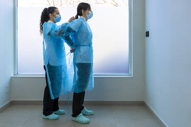 Nurse helping doctor in wearing protective workwear in hospital - DLTSF02842