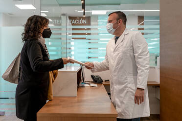 Doctor giving medical test report to patient at reception desk in pandemic - DLTSF02855