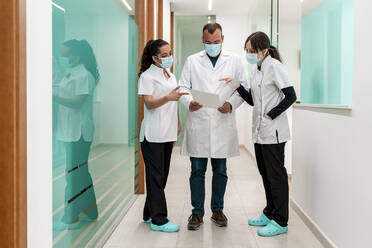 Doctor discussing medical report with nurses in corridor at hospital - DLTSF02873