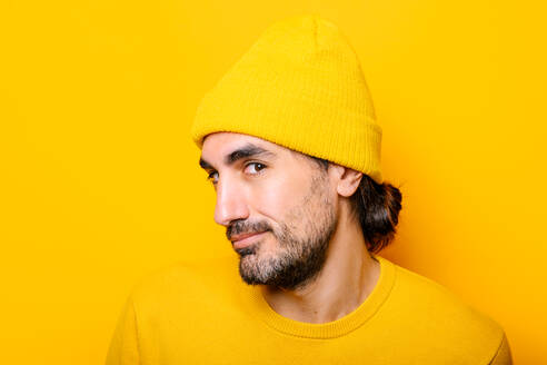 Happy bearded male with dark hair looking at camera while standing on yellow background in light studio - ADSF33968