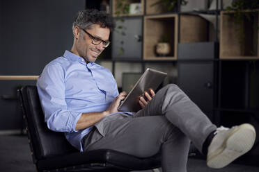 Smiling businessman wearing eyeglasses using tablet PC in office - RBF08626