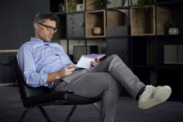 Businessman reading document sitting on chair in office - RBF08630