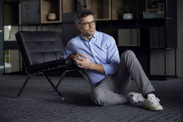 Businessman with hands clasped leaning on chair sitting in office - RBF08635