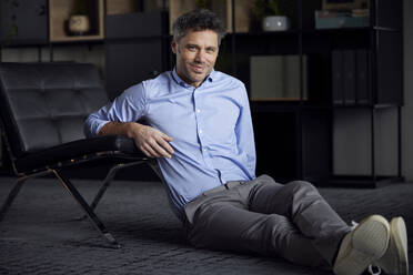 Smiling businessman leaning on chair sitting in office - RBF08636