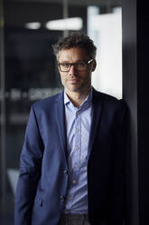 Businessman wearing eyeglasses standing in office - RBF08638