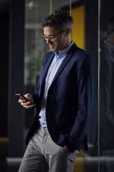 Businessman with hand in pocket using smart phone at work place - RBF08640