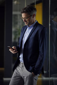 Geschäftsmann mit Hand in der Tasche bei der Nutzung eines Smartphones am Arbeitsplatz - RBF08640