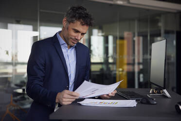 Geschäftsmann, der ein Dokument am Schreibtisch stehend im Büro liest - RBF08645