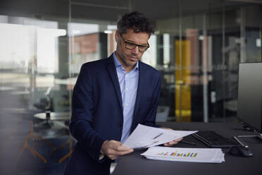 Geschäftsmann mit Brille, der ein Dokument am Schreibtisch im Büro liest - RBF08646