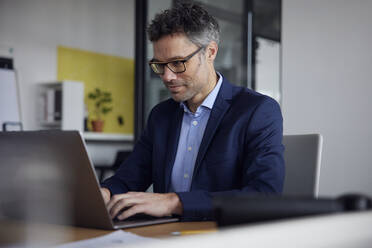 Businessman wearing eyeglasses using laptop at work place - RBF08647