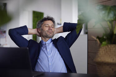Businessman with eyes closed sitting in office - RBF08668