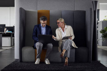 Businesswoman discussing with colleague using laptop sitting on sofa in office - RBF08682