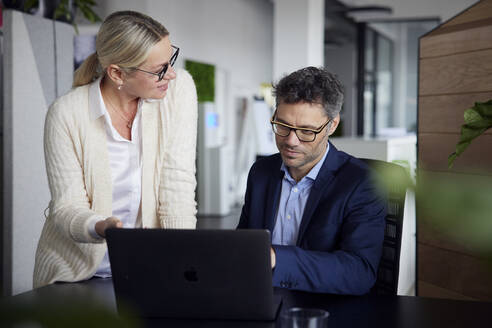 Geschäftsfrau tauscht Ideen mit einem Kollegen aus, der am Schreibtisch im Büro sitzt - RBF08684