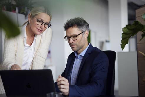 Geschäftsmann und Geschäftsfrau mit Brille teilen sich einen Laptop im Büro - RBF08685