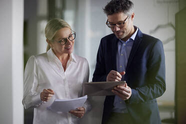 Smiling businesswoman holding document discussing with colleague using tablet PC in office - RBF08692