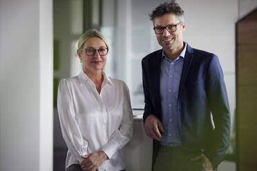 Smiling business colleagues wearing eyeglasses standing in office - RBF08693