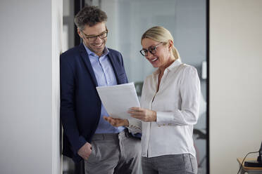Happy business colleague discussing document in office - RBF08696