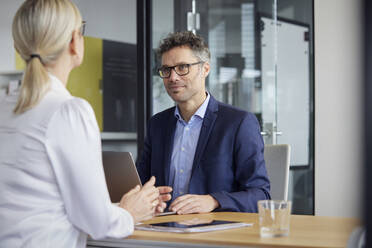 Business colleagues discussing with each other sitting at desk in office - RBF08699