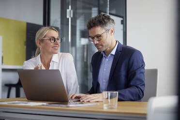 Lächelnde Geschäftsfrau, die ihren Kollegen bei der Arbeit am Laptop im Büro beobachtet - RBF08702