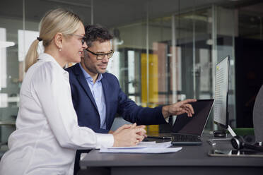 Businessman pointing at laptop screen sitting with colleague in office - RBF08713