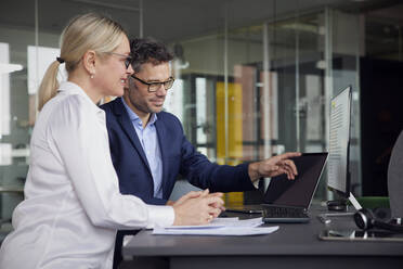 Geschäftsmann, der auf einen Laptop-Bildschirm zeigt und mit einem Kollegen im Büro sitzt - RBF08713