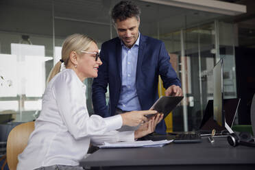 Businesswoman sharing tablet PC with colleague in office - RBF08716