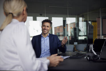 Lächelnder Geschäftsmann, der mit einem Kollegen im Büro diskutiert - RBF08718