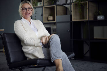 Happy businesswoman wearing eyeglasses sitting at work place - RBF08724