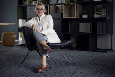 Lächelnde Geschäftsfrau sitzt auf einem Stuhl im Büro - RBF08725