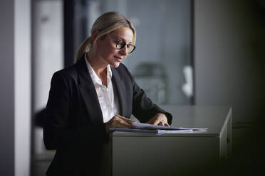 Geschäftsfrau beim Lesen von Dokumenten stehend am Schreibtisch im Büro - RBF08730
