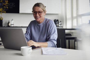 Glückliche Geschäftsfrau mit Laptop am Tisch - RBF08738