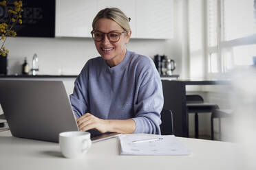 Happy businesswoman using laptop at table - RBF08738