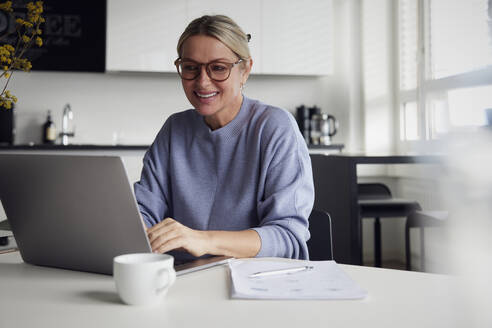 Glückliche Geschäftsfrau mit Laptop am Tisch - RBF08738