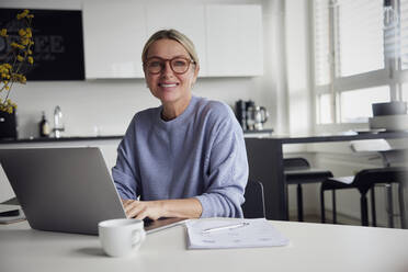 Smiling businesswoman with laptop sitting at table - RBF08739