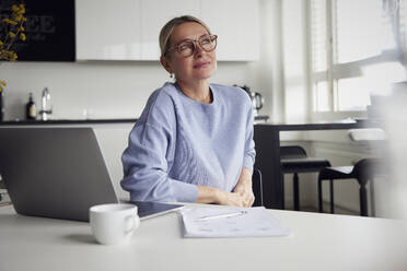 Contemplative businesswoman sitting with laptop at table - RBF08741