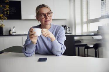 Businesswoman holding coffee cup sitting at table - RBF08742