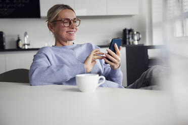 Happy businesswoman using smart phone sitting at table - RBF08744