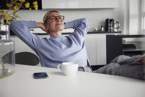 Geschäftsfrau mit Brille sitzt mit den Händen hinter dem Kopf am Tisch - RBF08745