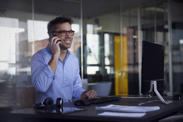 Smiling businessman talking on smart phone at work place - RBF08753