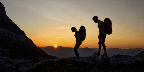 Silhouette eines Paares mit Rucksack, das bei Sonnenuntergang auf einem Berg wandert - ALRF01859