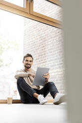 Man with tablet PC sitting in front of glass window - PESF03550