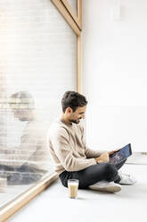 Man using tablet PC sitting cross-legged at home - PESF03554