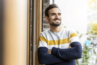 Smiling man with arms crossed leaning on door frame - PESF03559