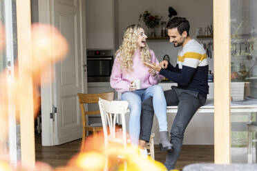 Playful couple sitting on table at home - PESF03566