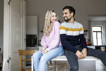 Boyfriend and girlfriend sitting on table at home - PESF03570