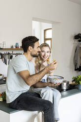 Couple eating noodles sitting on kitchen counter at home - PESF03583