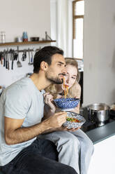 Boyfriend and girlfriend eating noodles in kitchen at home - PESF03584