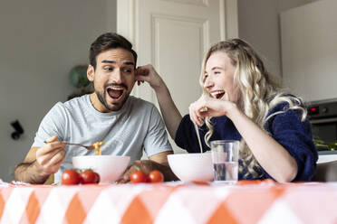 Playful couple eating food on dining table at home - PESF03590