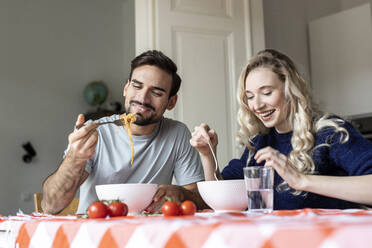 Man and woman eating food sitting on dining table at home - PESF03591