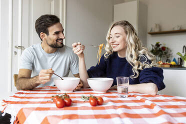 Couple eating food together on dining table at home - PESF03593